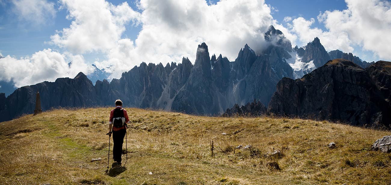 Persona con bastoni da camminata su prato con Dolomiti sullo sfondo